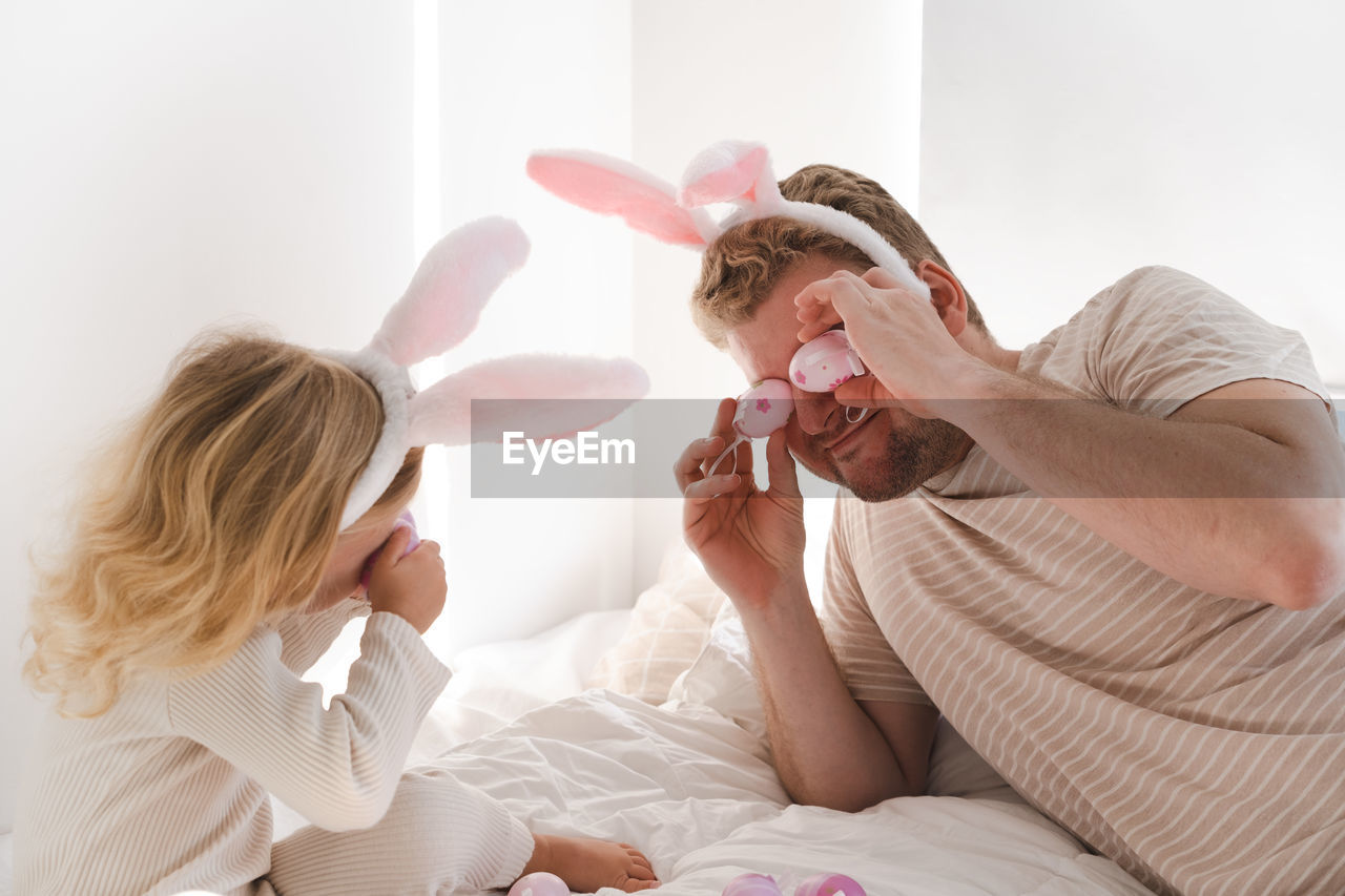 Father and daughter at home celebrating easter wearing rabbit ears playing with eggs