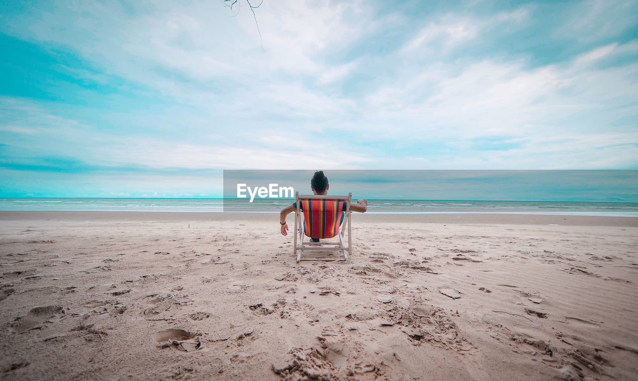 Rear view of man relaxing on beach against sky