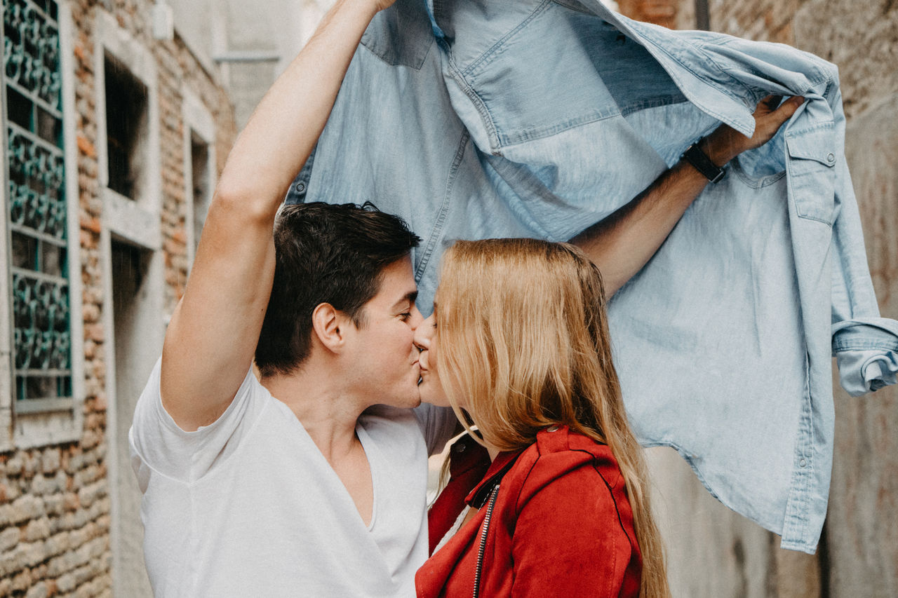 Young couple kissing under jacket against wall