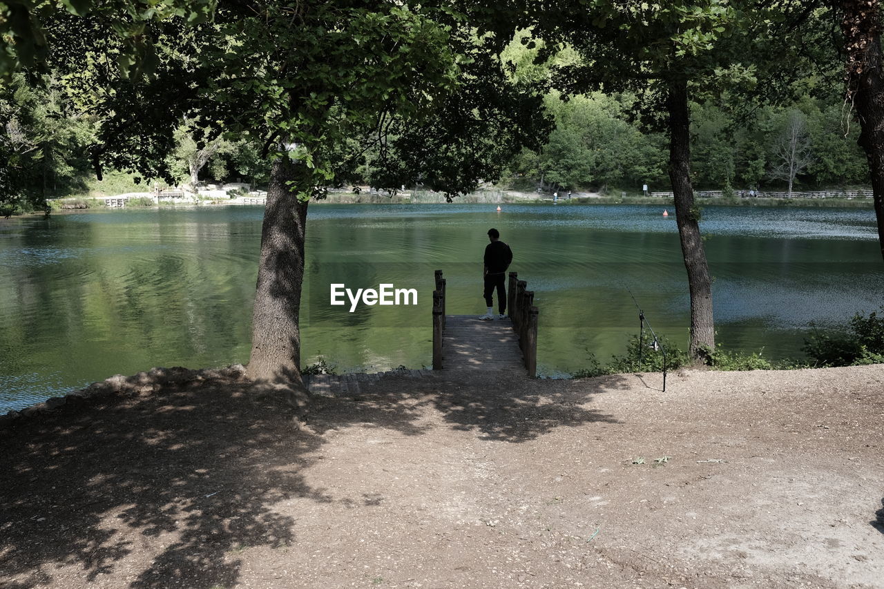 Rear view of silhouette man standing on pier by trees at lago sinizzo lake