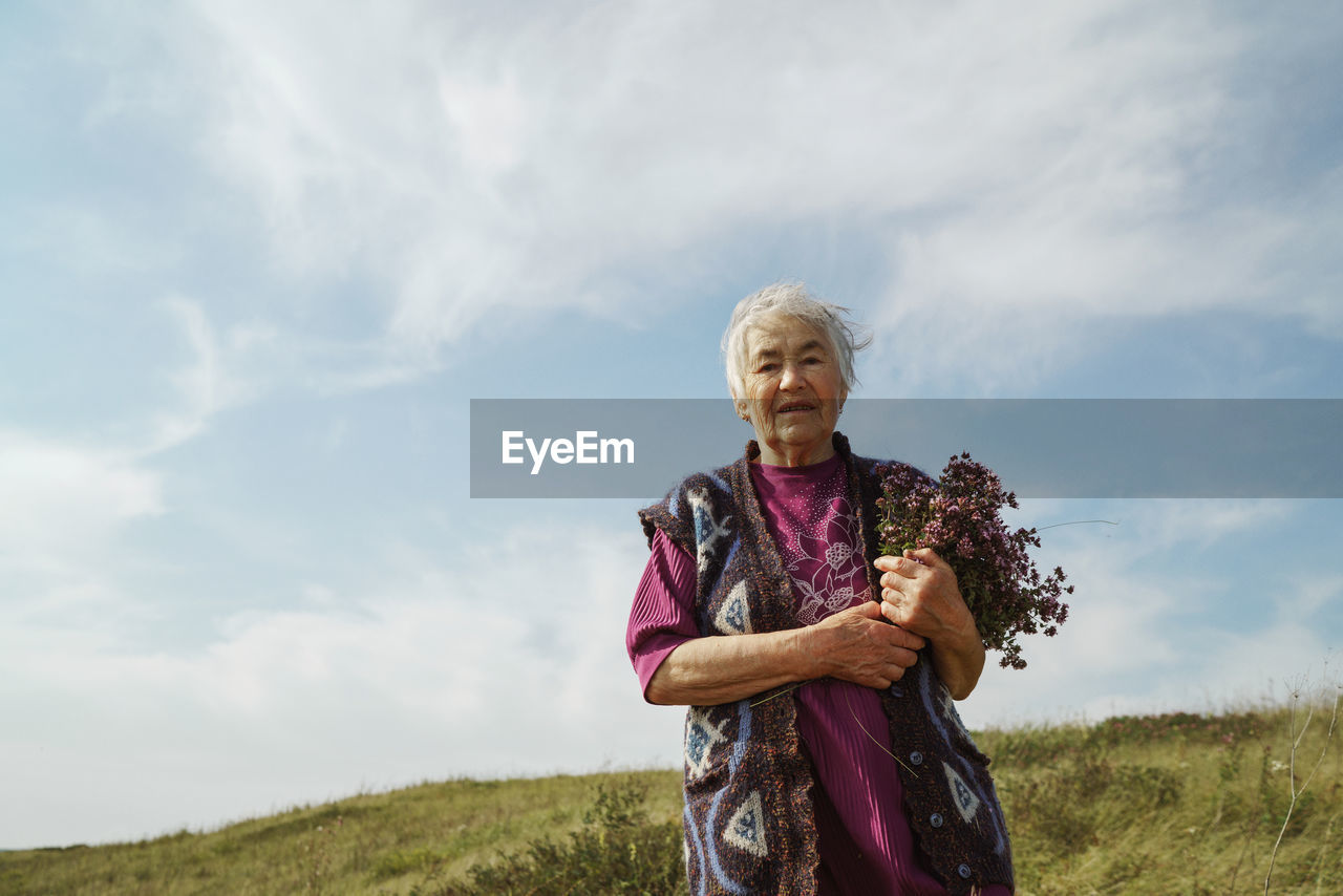 Amature woman holding bouquet of flowers standing on field against sky