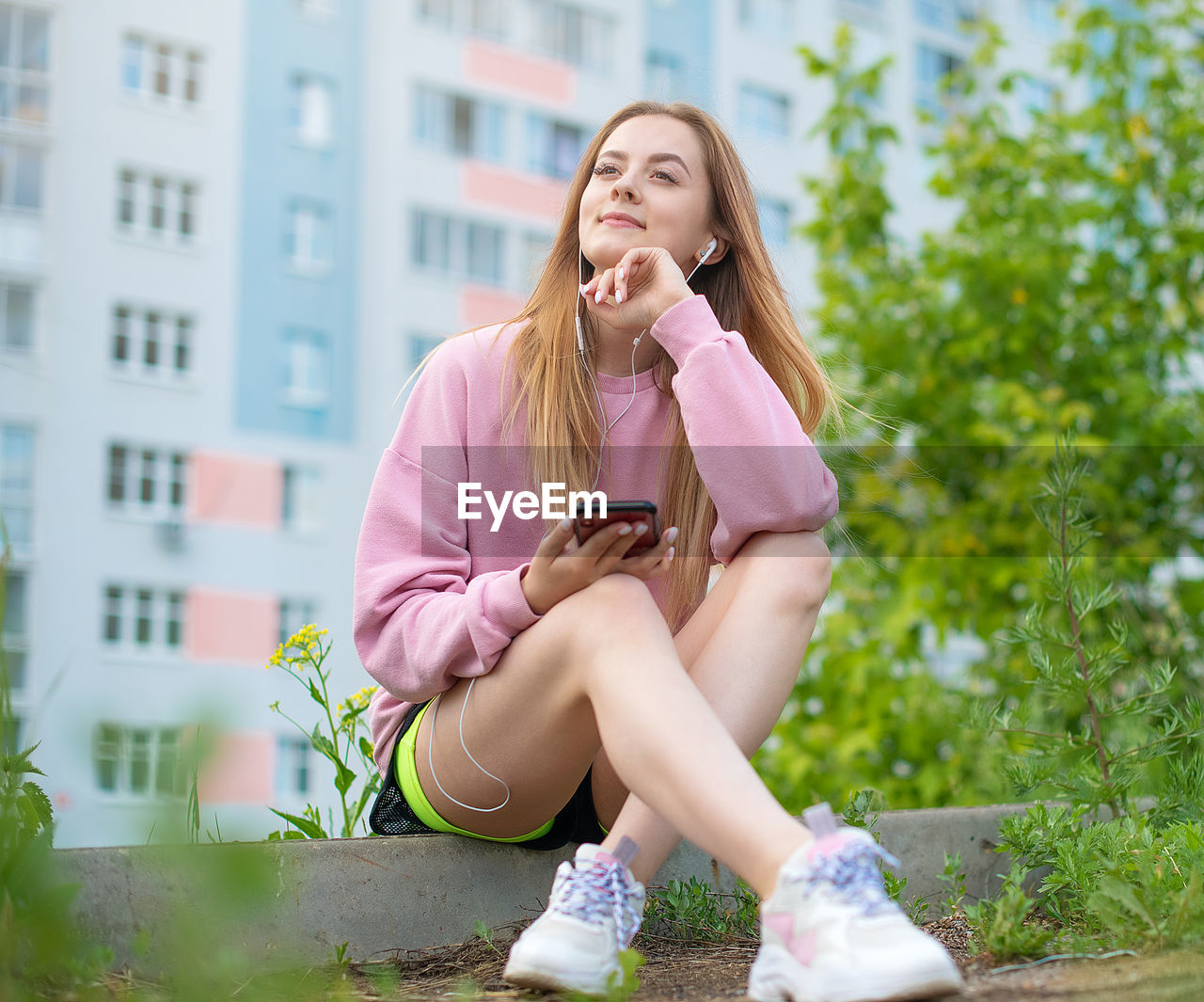 FULL LENGTH OF WOMAN USING MOBILE PHONE WHILE SITTING ON CAMERA OUTDOORS