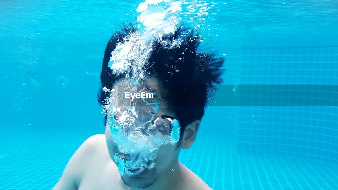 Young man swimming underwater in pool