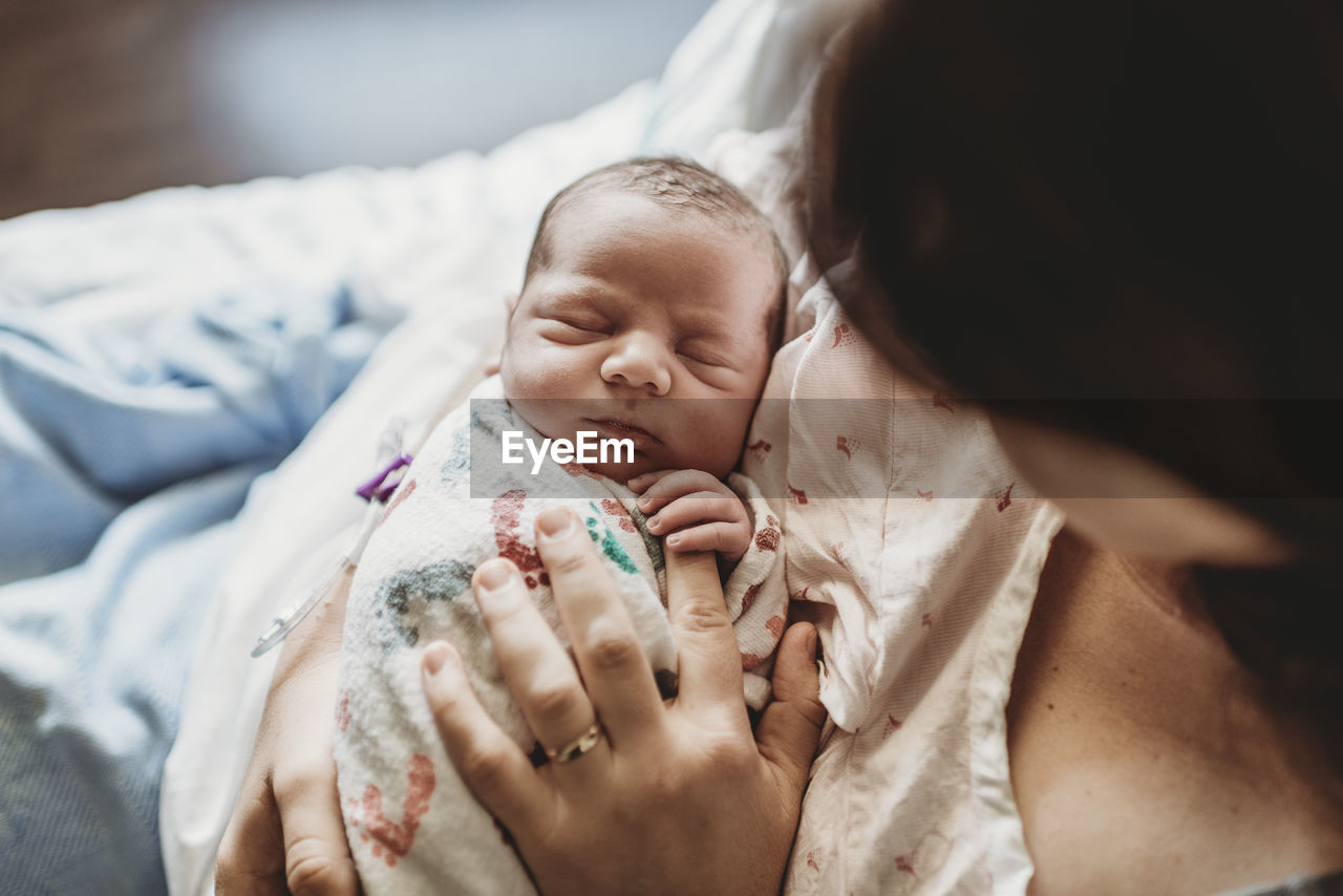 Overhead view of mother holding newborn boy's fingers in hospital bed