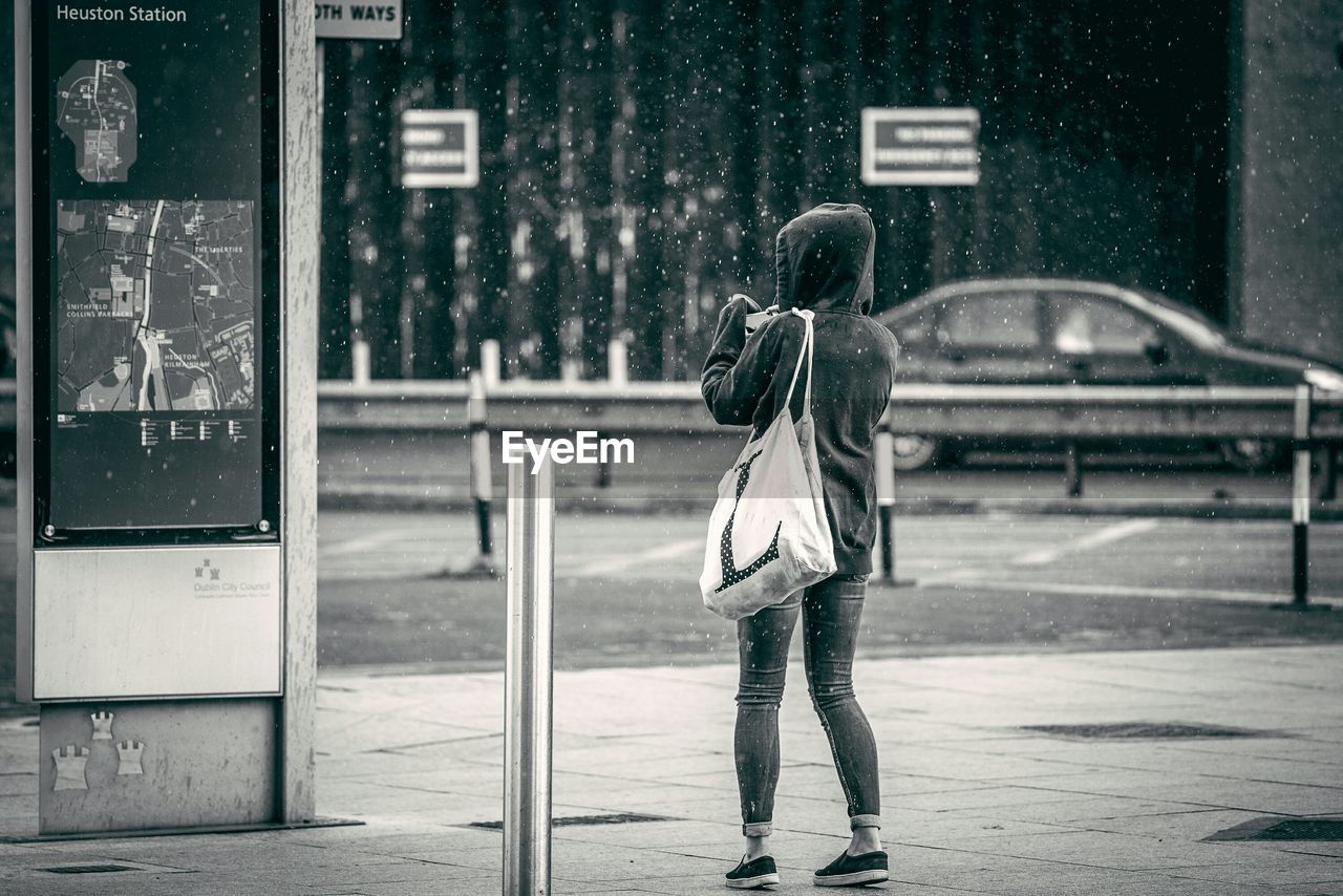 Rear view of woman standing in rain on footpath