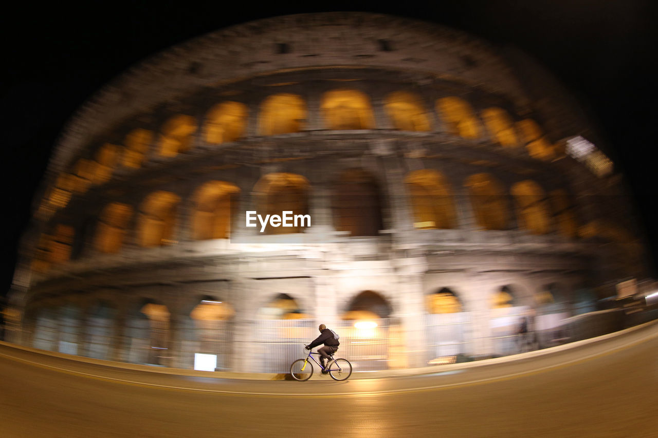 Low angle view of man riding bicycle against coliseum at night