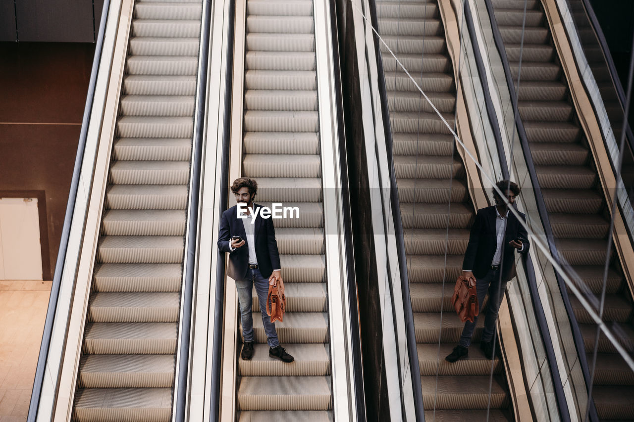 Businessman holding bag moving down from escalator