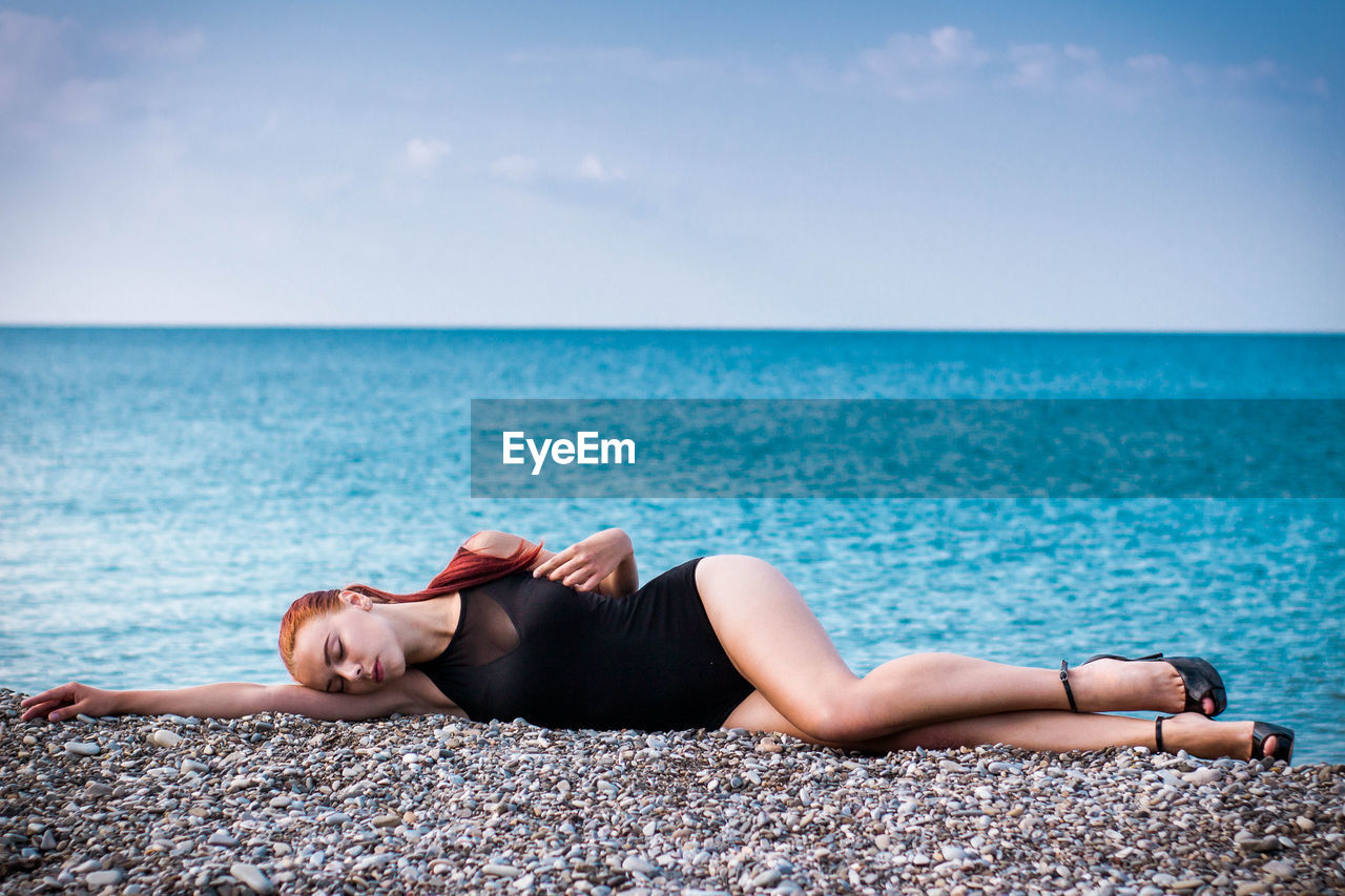 Full length of sensuous woman in swimwear lying down at beach