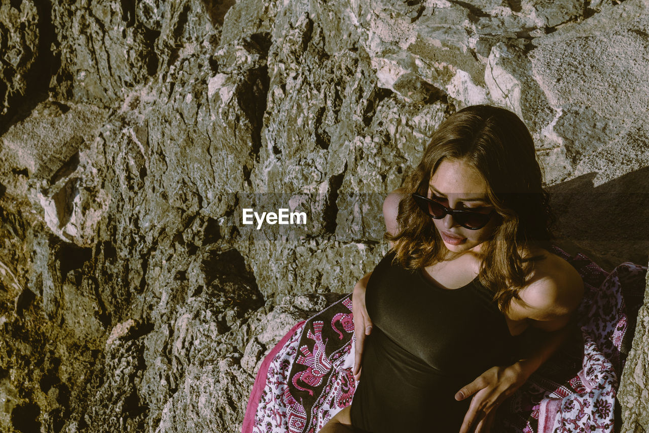 High angle view of woman wearing sunglasses sitting on rock formation