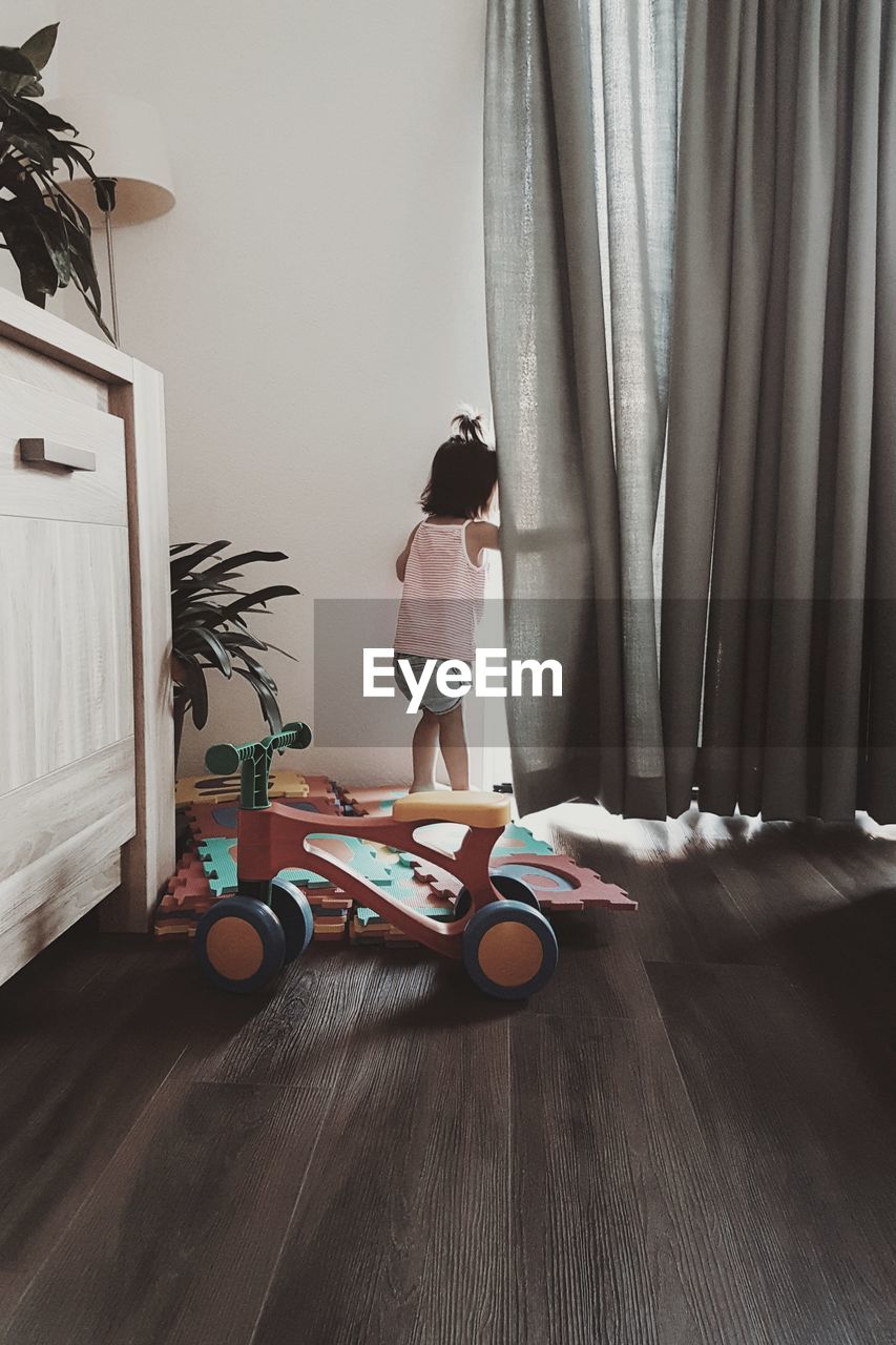 Rear view of baby girl standing by curtain at home