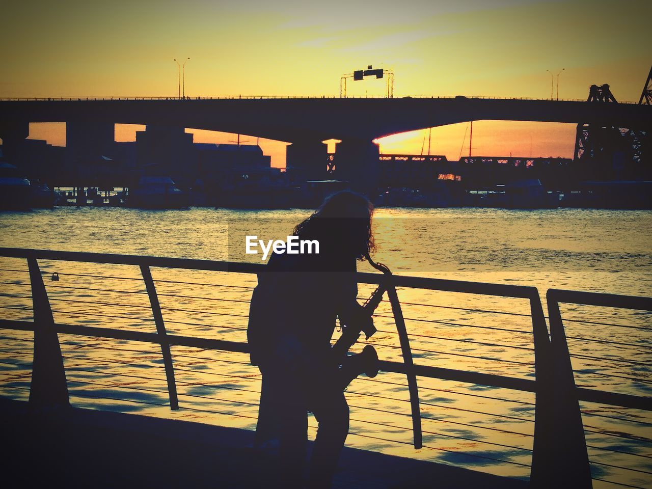 SILHOUETTE MAN STANDING ON BRIDGE AGAINST SUNSET SKY