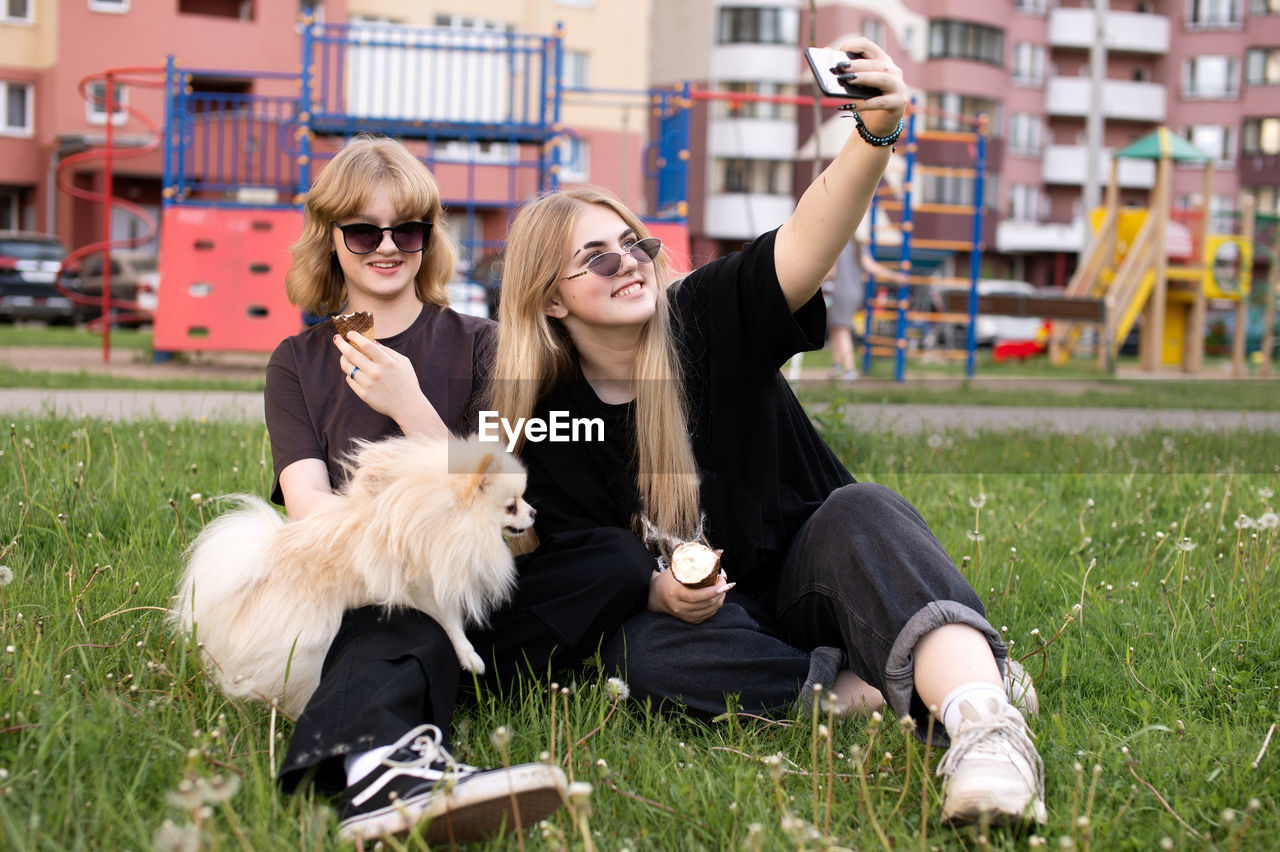 Two funny girls are eating ice cream and playing with a pomeranian dog. taking selfies