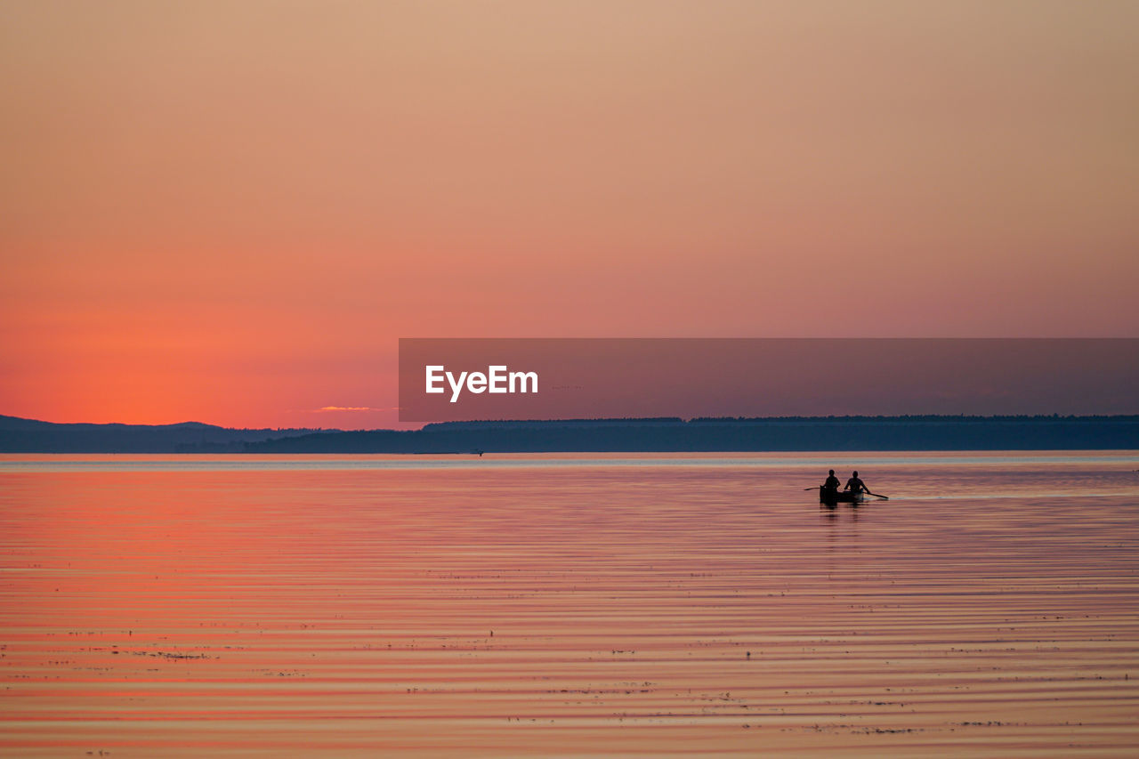 Silhouette people on boat in sea against orange sky