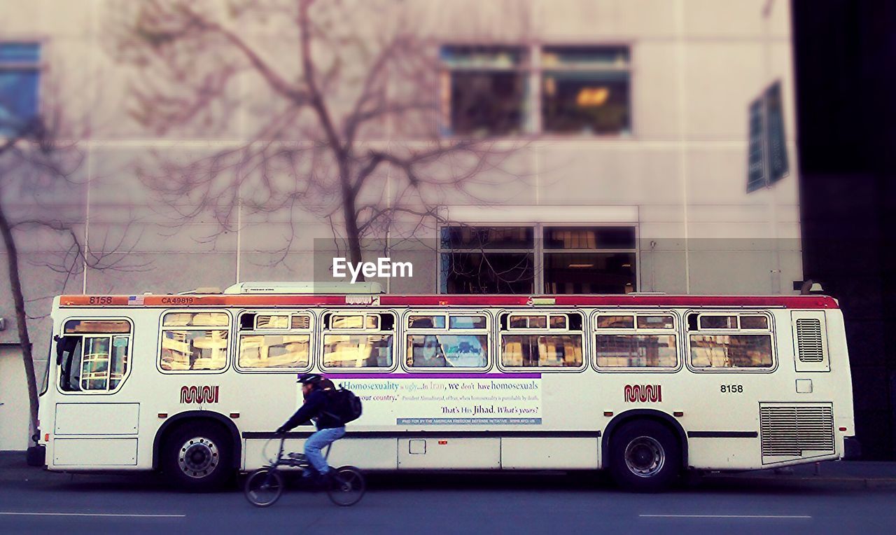 Man riding bicycle by bus on city street