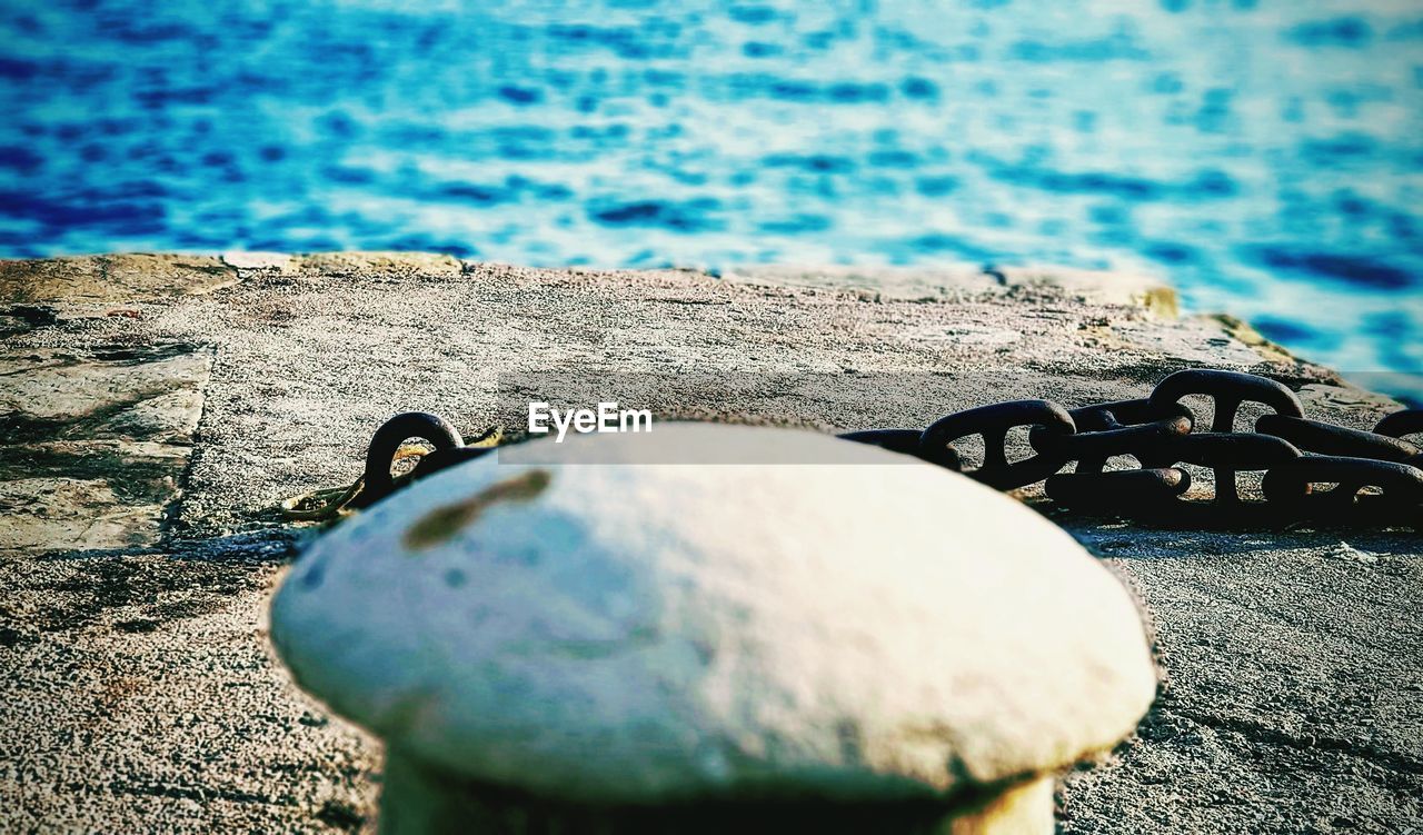 Close-up of bollard and chain on retaining wall by sea