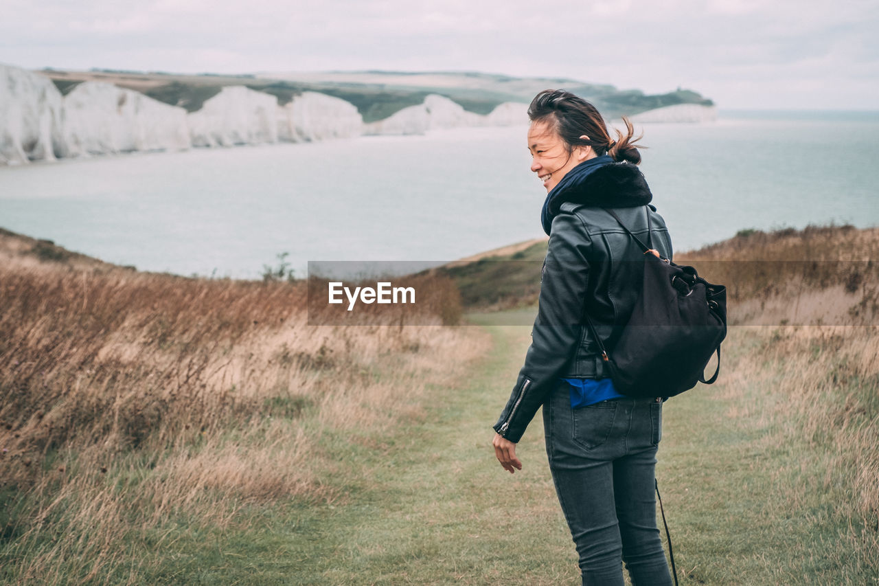 Asian woman laughing while trekking on a cliff by the sea