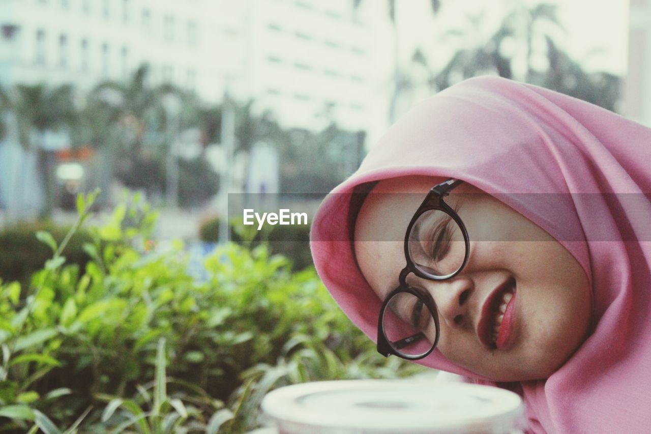 Close-up portrait of woman winking against plants