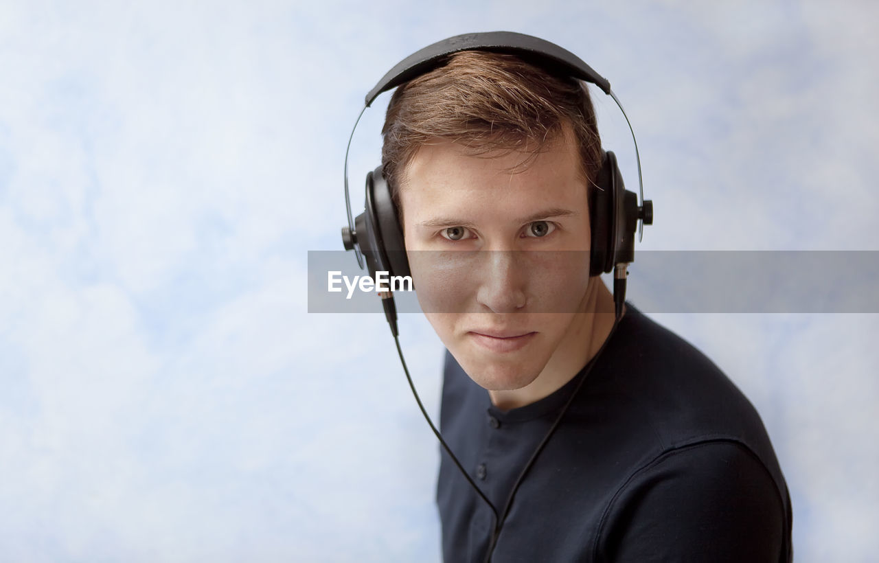 Portrait of young man wearing headphones against sky