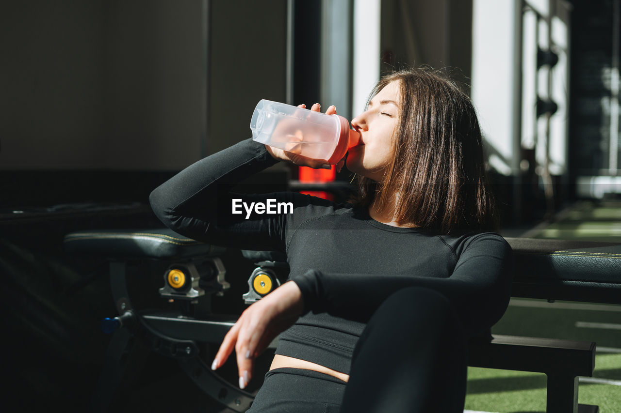 Portrait of resting young brunette woman in sport active wear drinking water in the fitness club