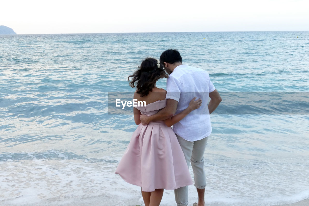 REAR VIEW OF FRIENDS STANDING ON BEACH