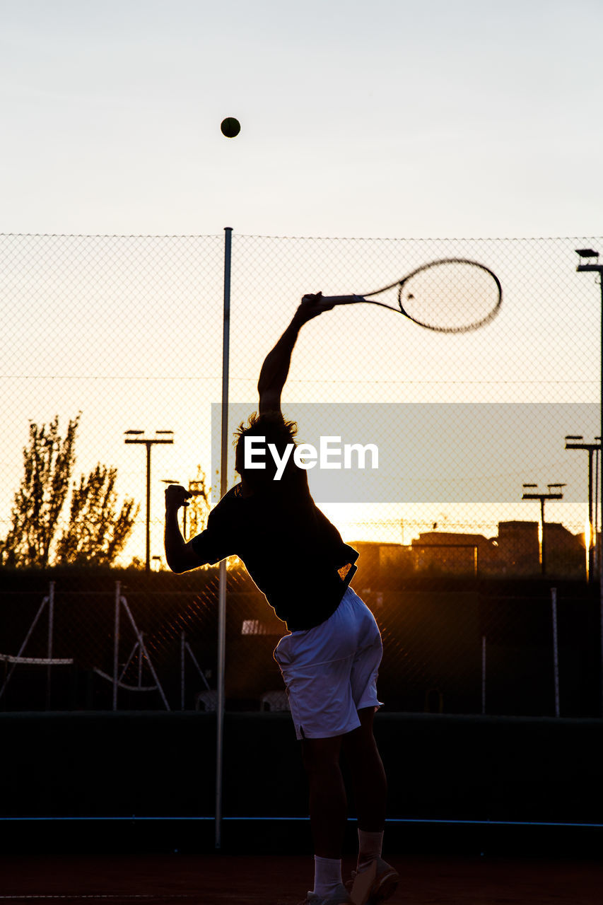 Full length of man playing tennis in court during sunset