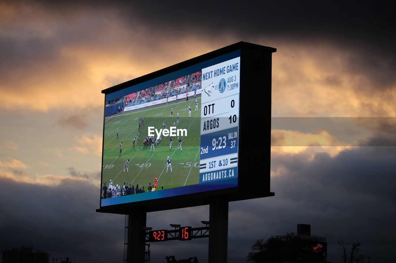 Low angle view of billboard against cloudy sky during sunset