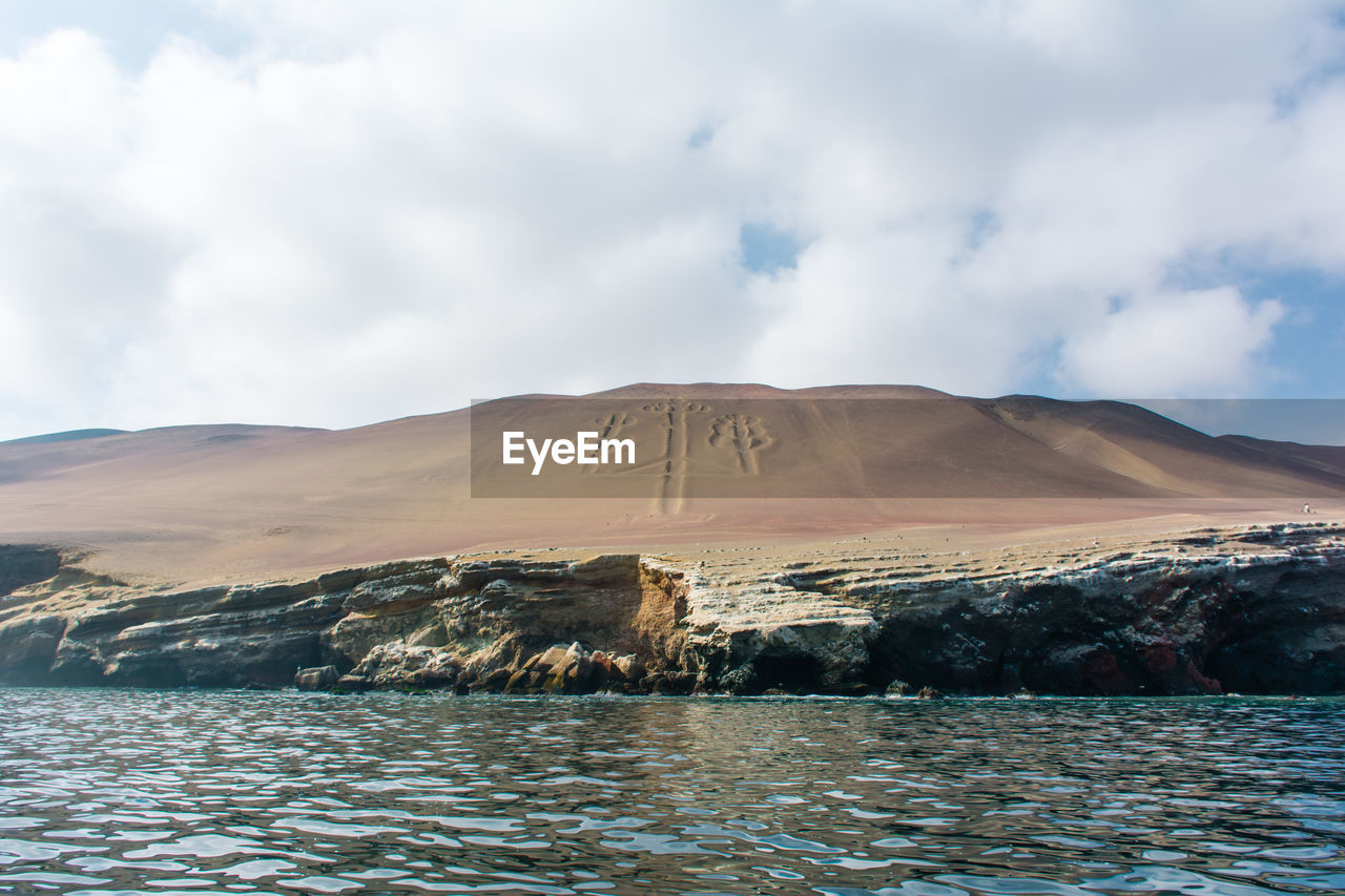 Scenic view of river by sand dunes against cloudy sky