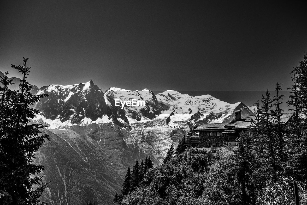 snow, tree, mountain, plant, cold temperature, winter, scenics - nature, nature, beauty in nature, black and white, sky, monochrome, mountain range, no people, darkness, monochrome photography, environment, architecture, snowcapped mountain, landscape, land, built structure, pinaceae, coniferous tree, tranquility, tranquil scene, building exterior, travel destinations, building, outdoors, pine tree, forest, travel, non-urban scene, day, house