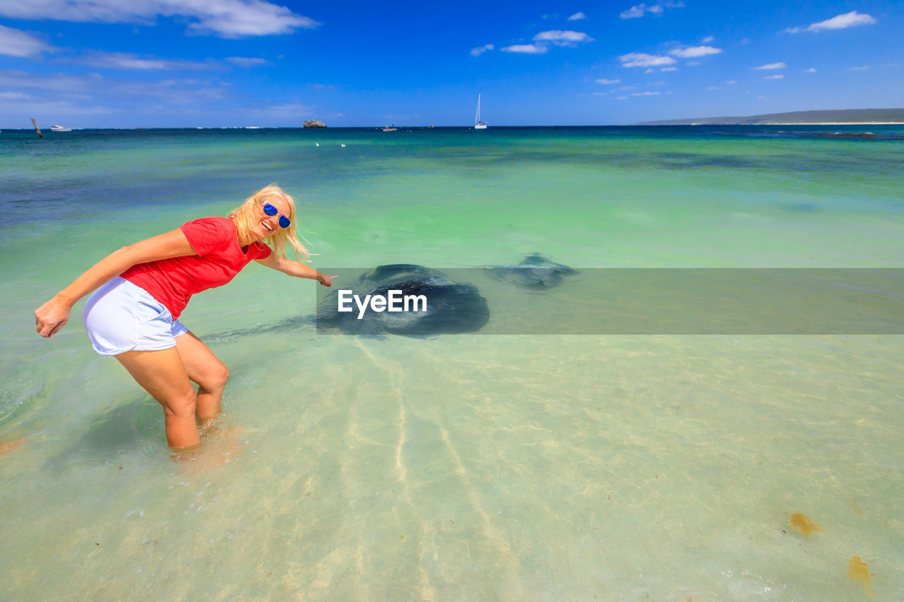 Portrait of woman pointing at stingray in sea