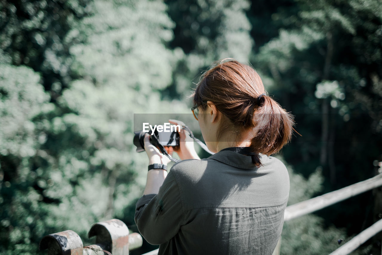 Woman photographing through camera while standing by railing on bridge