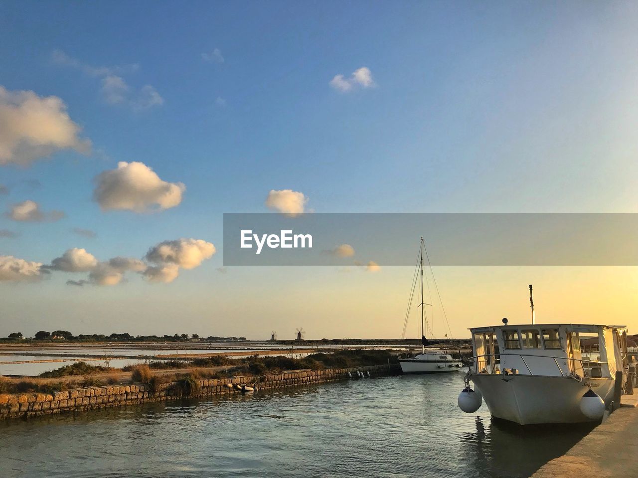 Sailboats moored at harbor against sky during sunset