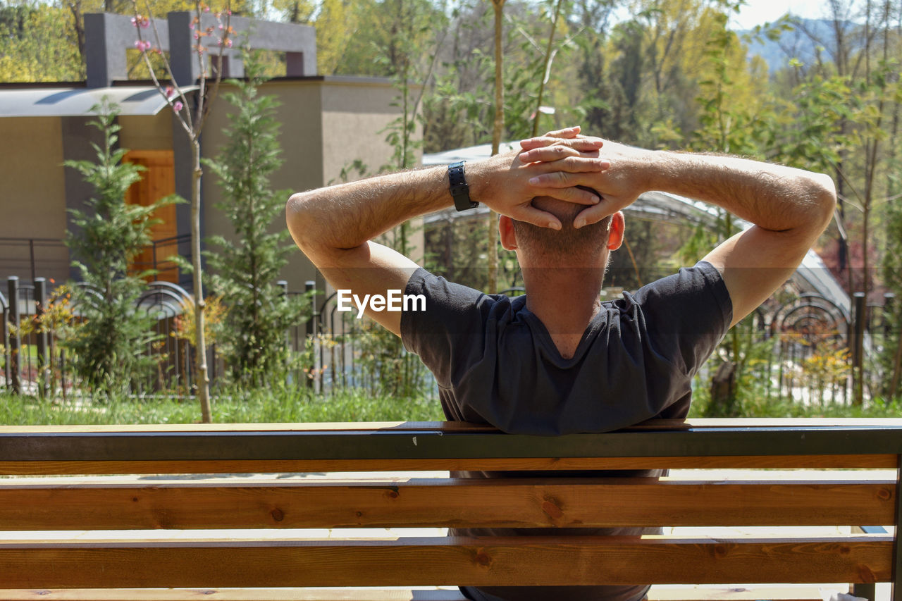 Man sitting with hands behind head while sitting on bench