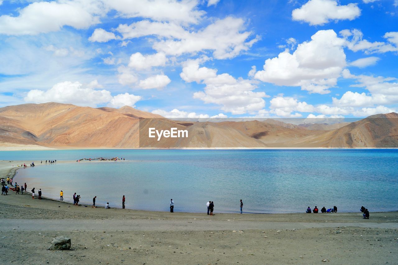 People by lake against mountain range