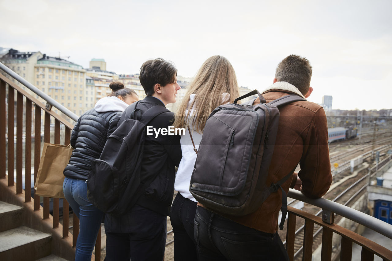 Teenage male and female friends leaning on railing of staircase in city