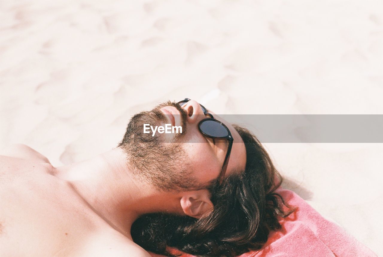 High angle view of shirtless young man lying on sand at beach during sunny day