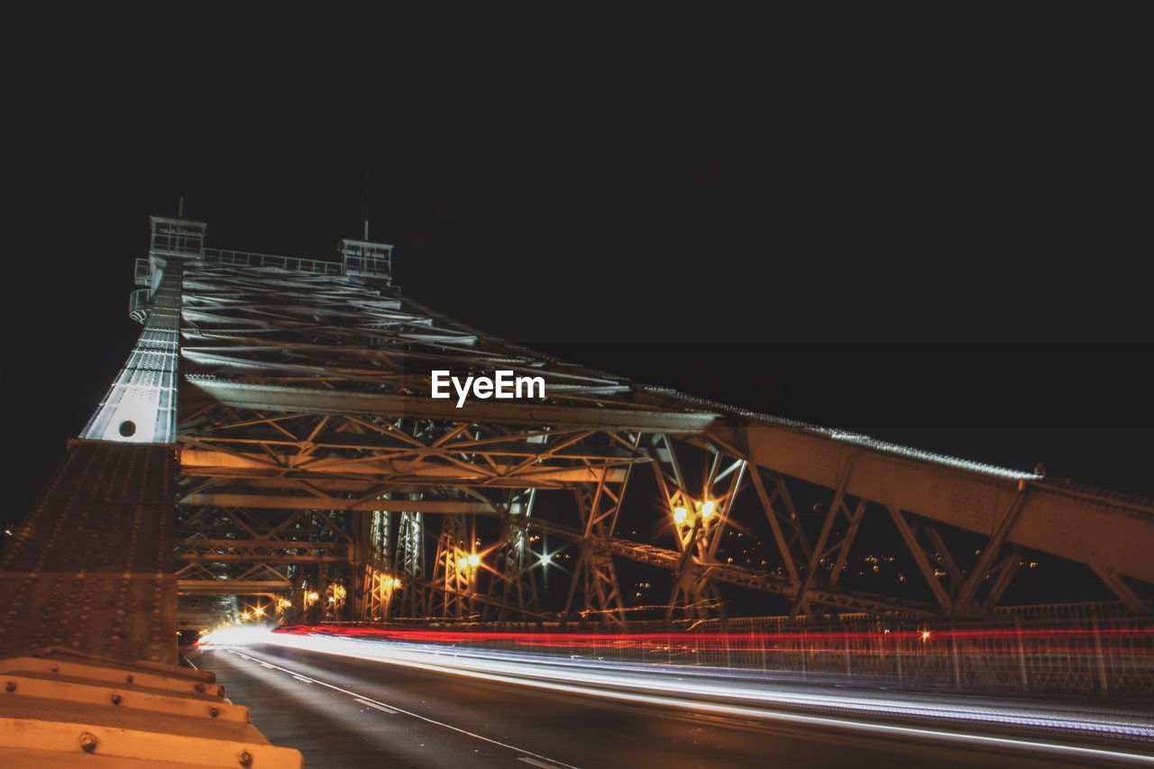 Light trails on bridge in city against sky at night