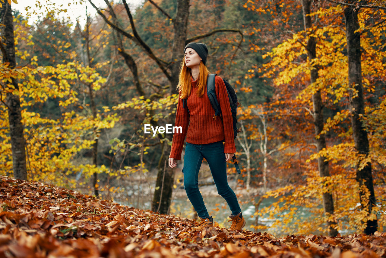 Full length of young woman standing amidst trees during autumn