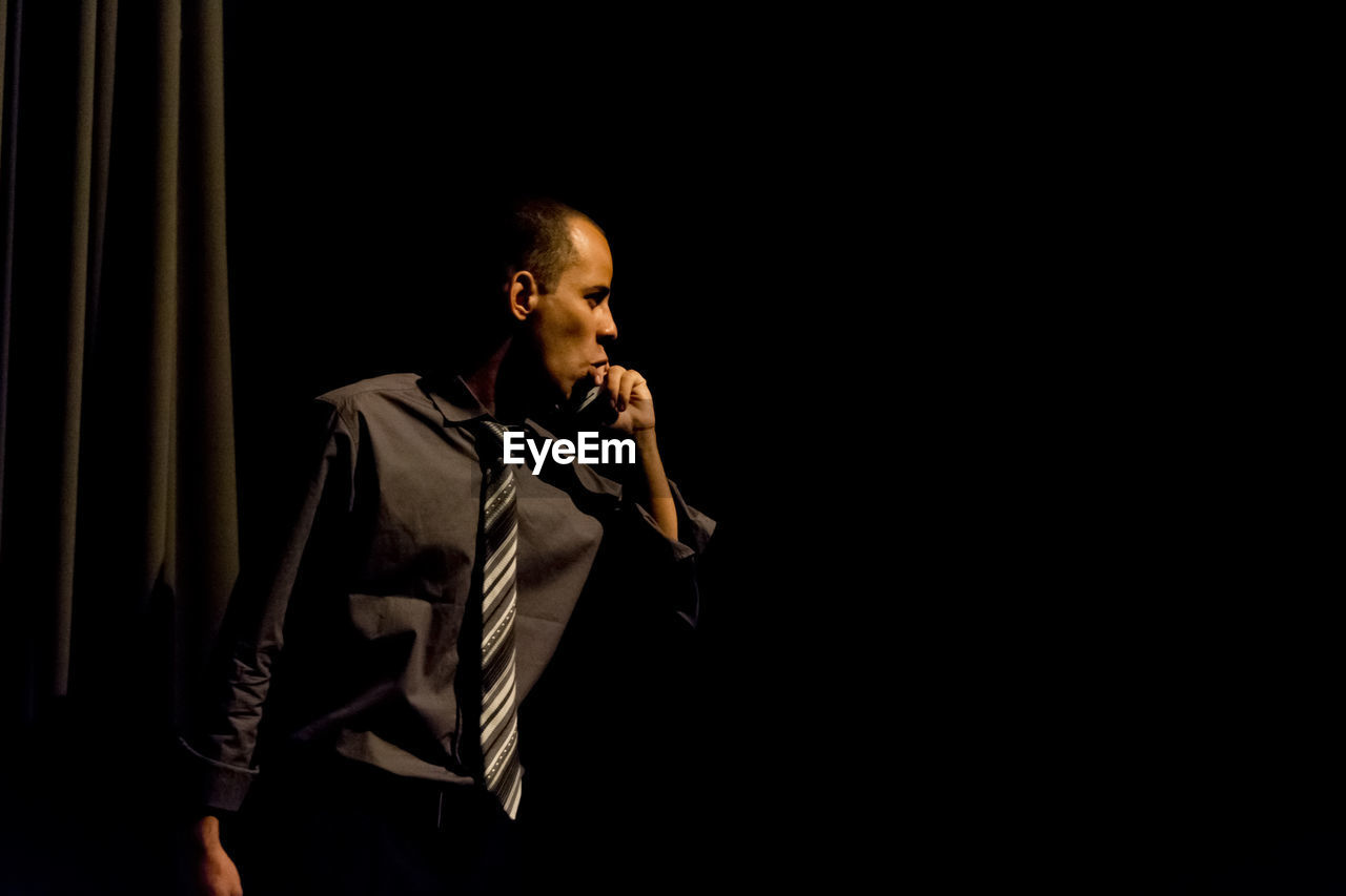 Young man looking away while standing against black background