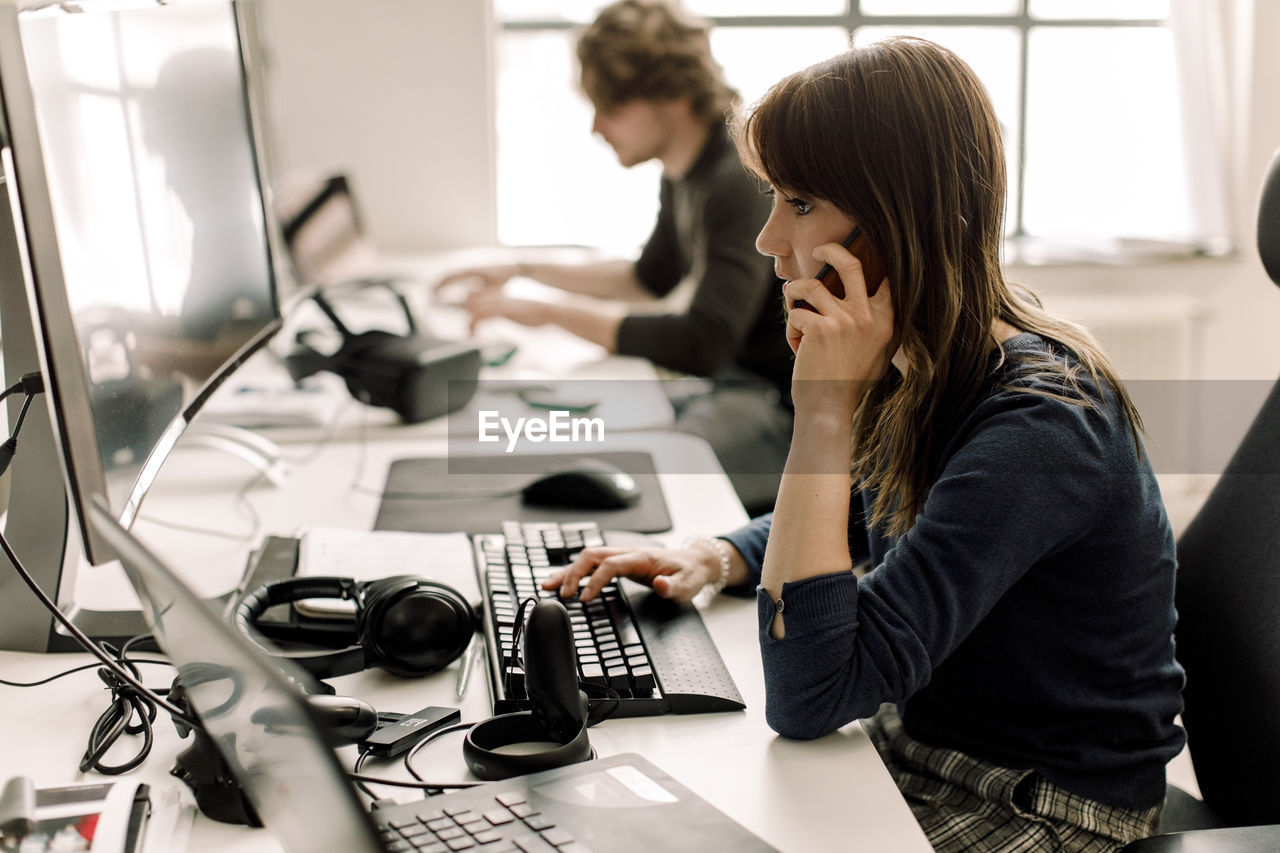 Female entrepreneur working on computer while talking on phone at workplace