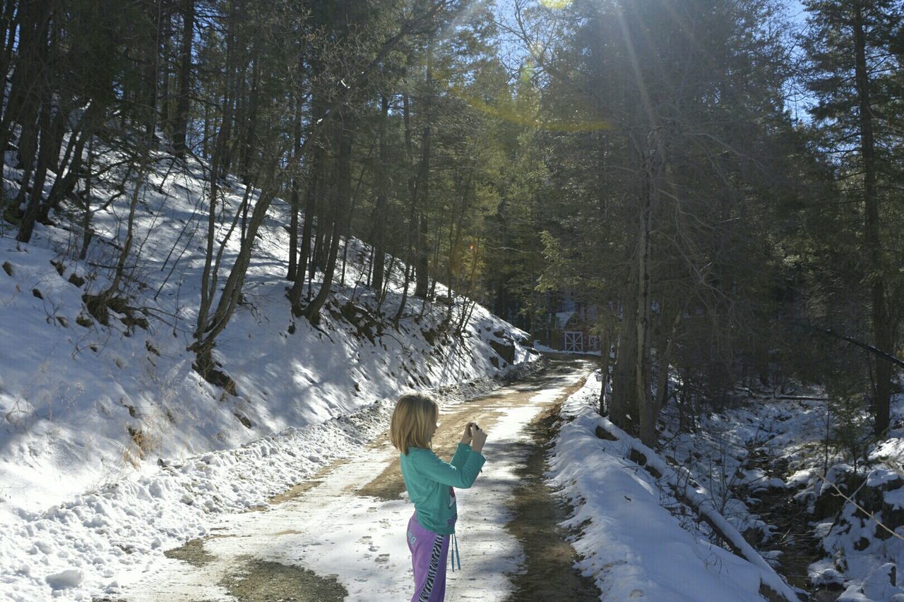 Side view of girl photographing in snow covered forest