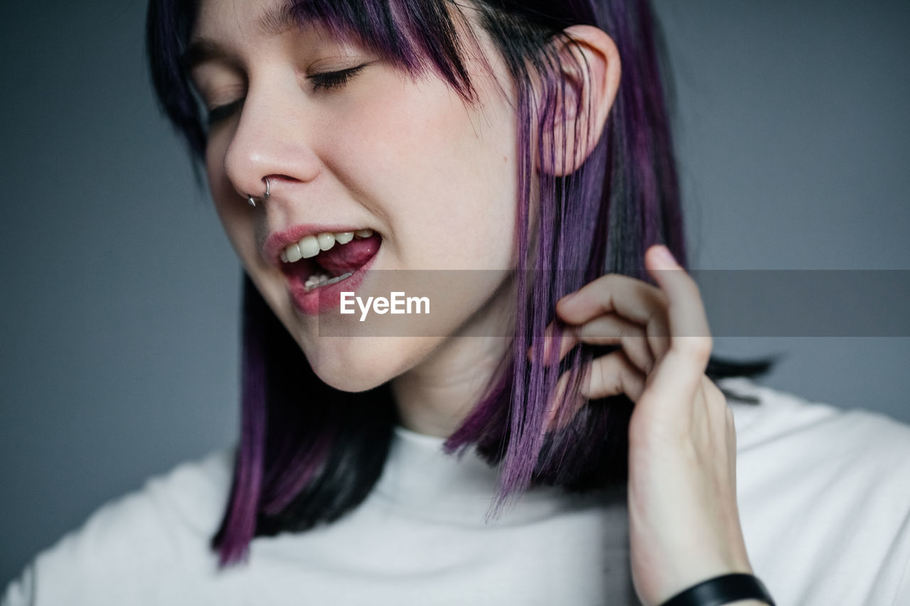 Portrait of a cheerful young girl with purple hair close-up on a gray background