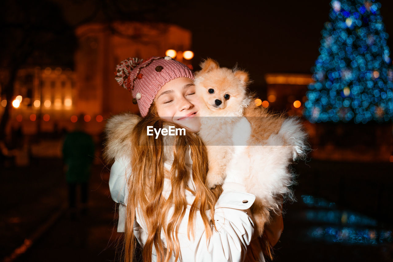 Cute girl holds spitz in her arms in evening on street in light of street