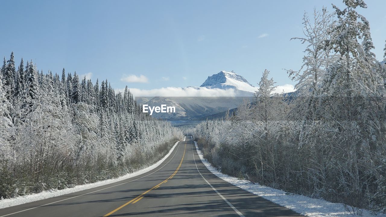 Empty road amidst snow covered mountains against sky