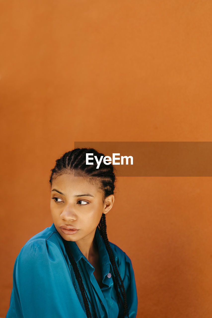 Young woman looking away by orange wall