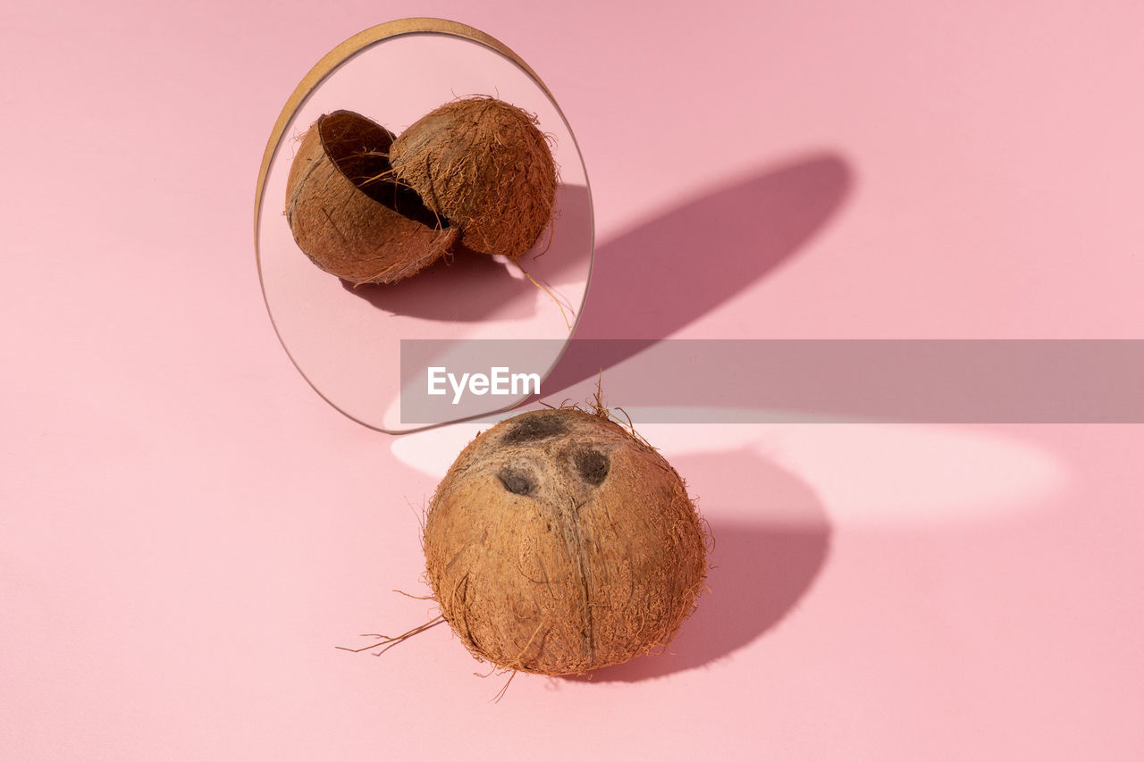 Coconut in a mirror with a broken reflection. creative food or broken concept. pink background