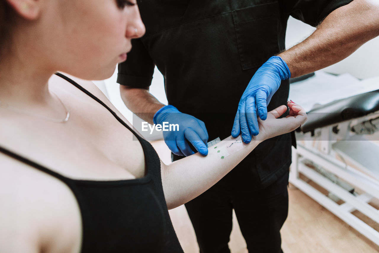 Crop anonymous male tattooist in latex gloves wiping freshly made tattoo on arm of female client with napkin while working in salon