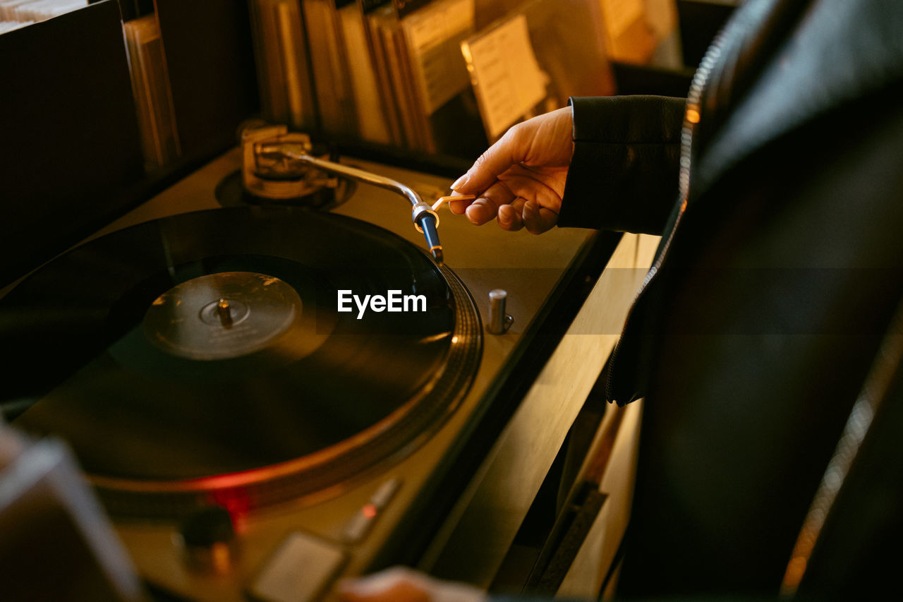 Crop anonymous person in leather jacket listening to song via vintage record player with vinyl disc while standing in store person