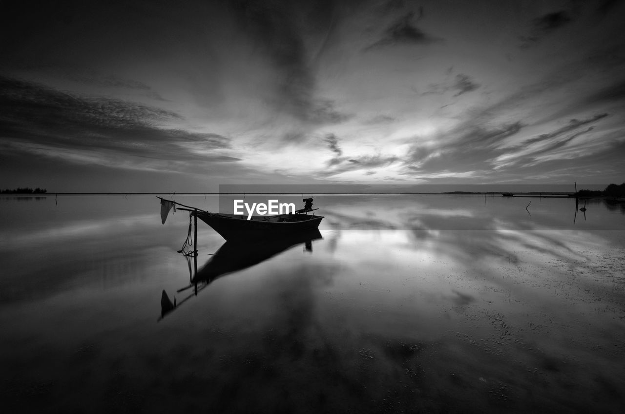 Fishing boat moored in sea against sky during sunset