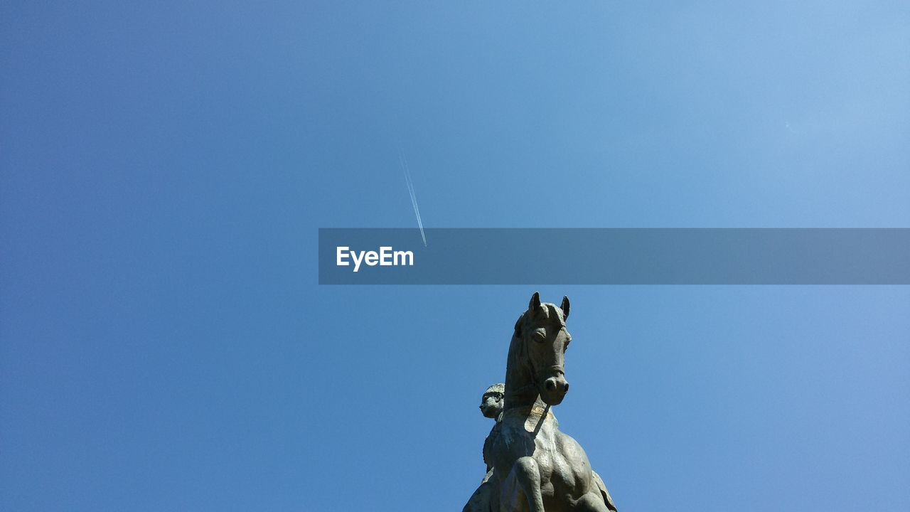 Low angle view of horse statue against blue sky