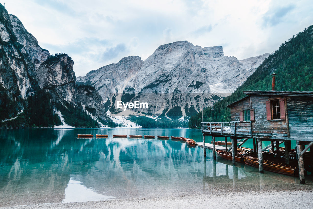 Majestic scenery of wooden house located on shore of clear lake with turquoise water and boats floating on smooth surface on background of mountains in morning light